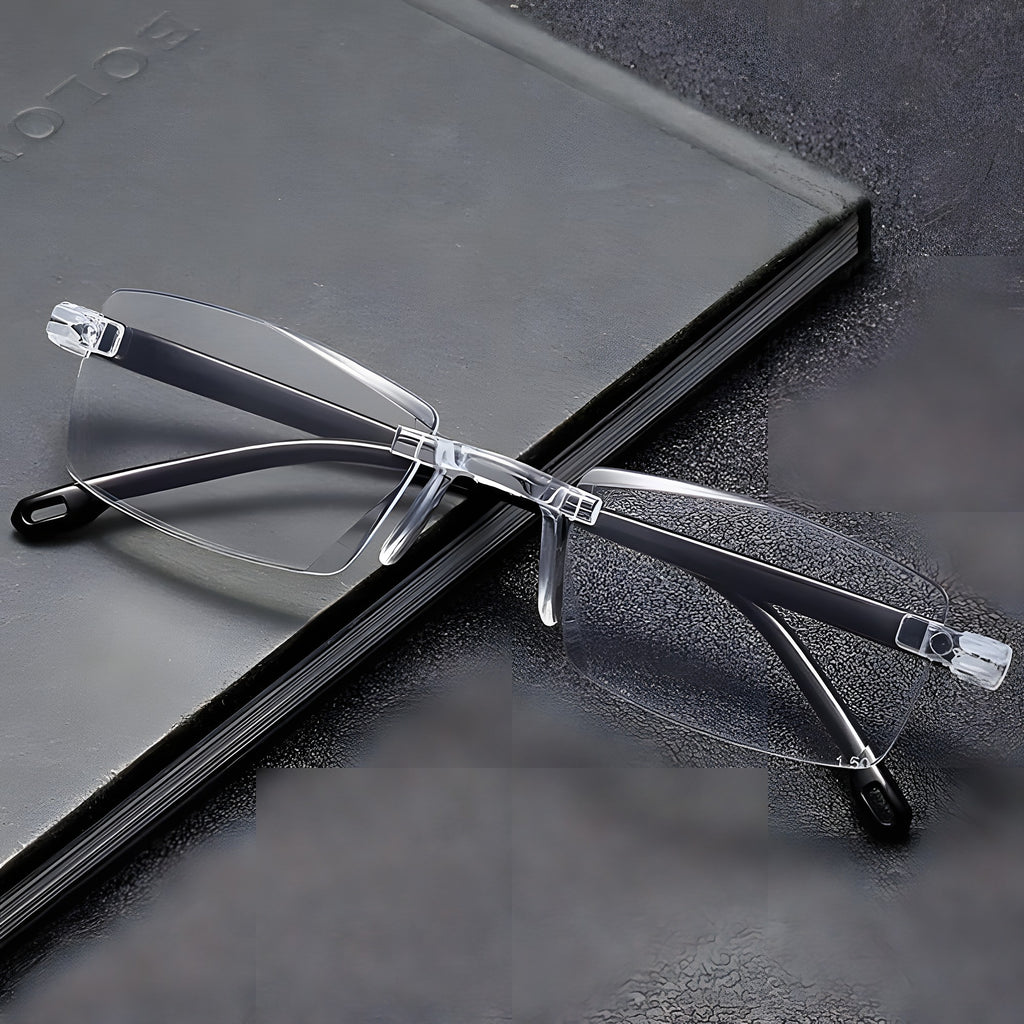 Clear rimless reading glasses with black temple arms on a grey notebook