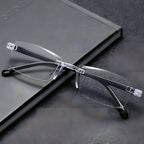 Clear rimless reading glasses with black temple arms on a grey notebook