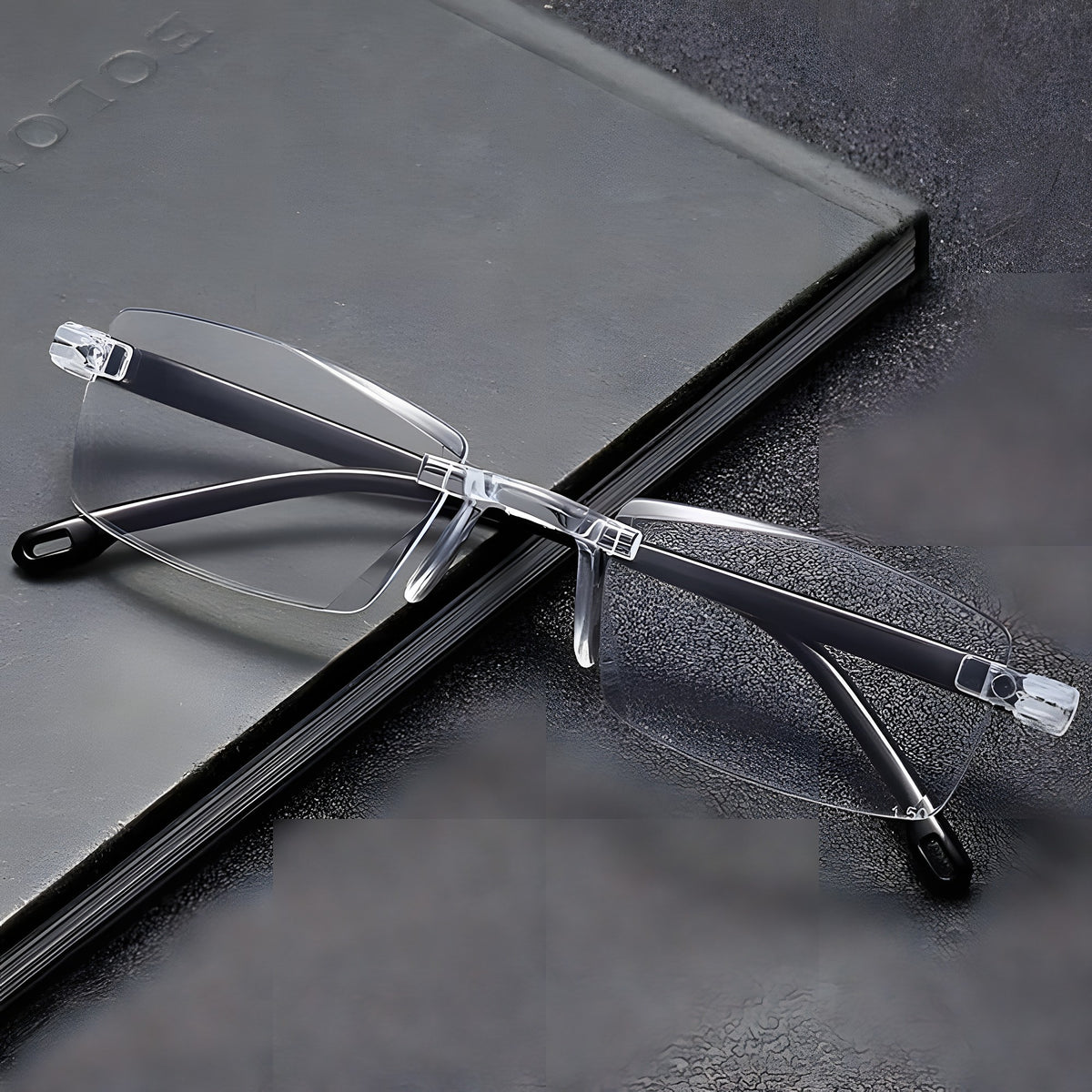 Clear rimless reading glasses with black temple arms on a grey notebook